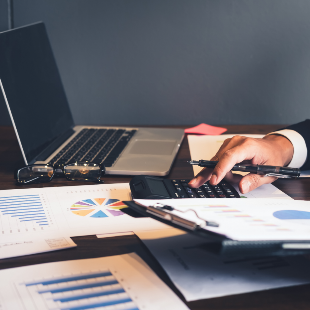 darbo stalas su kompiuteriu ir vyro ranka, laikanti rašiklį